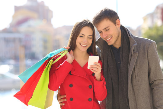 Tourists consulting phone holding shopping bags in winter