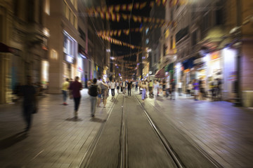 Naklejka na ściany i meble Blurry motion image of people walking in Istiklal Avenue (the city’s main pedestrian boulevard) at night in Istanbul. The street which is lined with 19th-century buildings, shopping chains and cafes.