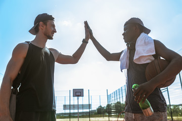 Obraz premium Side view portrait of two basketball players doing high-five against blue sky after match in outdoor court, copy space