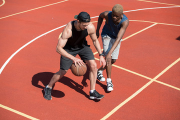 High angle action shot of two handsome  muscular men playing basketball in outdoor court lit by...