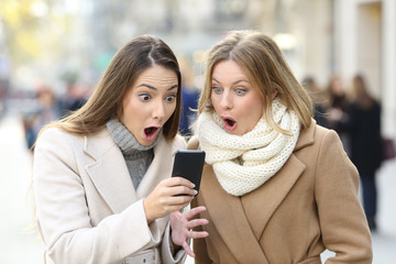 Surprised women reading phone content in winter in the street