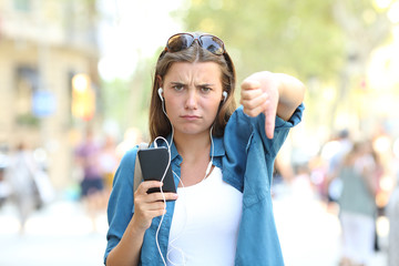 Annoyed girl listening to music with thumbs down