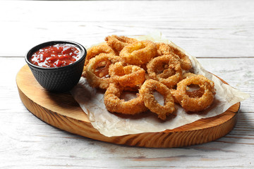 Homemade crunchy fried onion rings with tomato sauce on wooden table