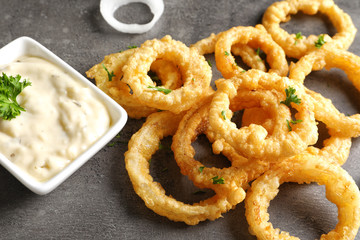 Naklejka premium Homemade crunchy fried onion rings with sauce on color table, closeup