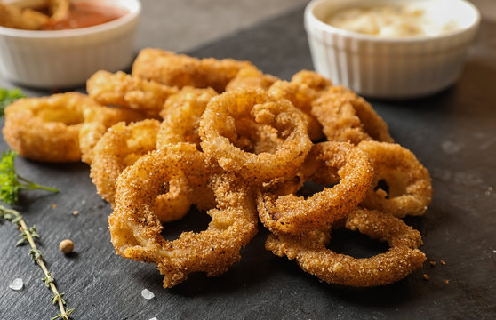 Homemade crunchy fried onion rings and sauces and sauces on slate plate, closeup