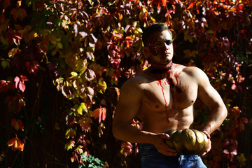 Man play with pumpkins and treat. Muscular boy with a beautiful neck holds pumpkin. Halloween...