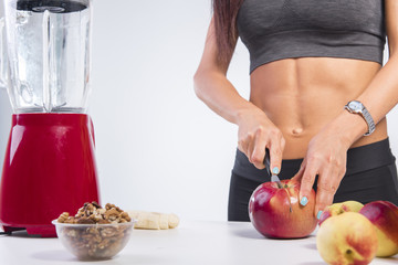 Young sportswoman making a delicious smoothie, mixing fruit and vegetarian ingredients, cutting an apple, studio white background