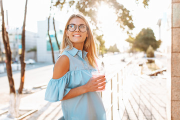 Portrait of a beautiful young girl student, wearing glasses, walking around the city with a cocktail in her hands
