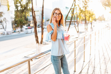 Portrait of a beautiful girl student, wearing glasses, talking on the phone in a good mood, and holding a cocktail