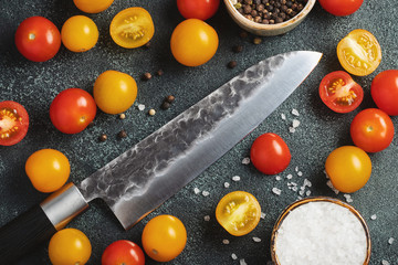Vintage chef knife next to red and yellow cherry tomatoes on a dark background. The concept of cooking. Top view. flat lay