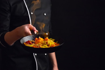 Professional chef and fire. Cooking vegetables and food over an open fire on a dark background....