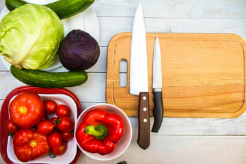 Set of various vegetables, healthy food products (tomatoes, sweet pepper, cabbage, cucumbers) and cutting board with knives.