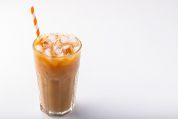 Ice coffee in a tall glass with cream poured over and coffee beans. Cold summer drink on white background with copy space