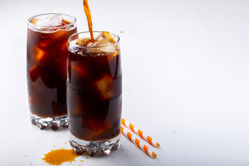Ice coffee in a tall glass with cream poured over and coffee beans. Cold summer drink on white background with copy space