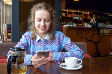 smiling woman using smartphone in coffee shop in cafe with cup of coffee
