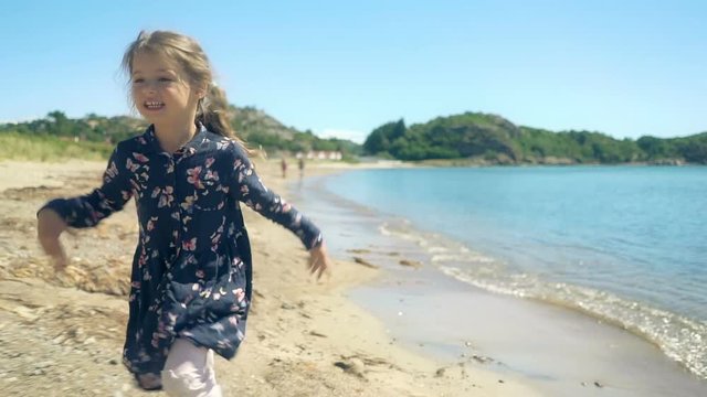 Little girl runs along a deserted northern beach on a sunny summer day. Slow motion