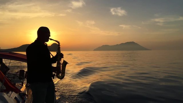 Bald Saxophonist plays on a floating yacht against the sunset
