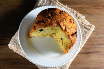 closeup panettone on ceramic plate on wooden table, towel underneath