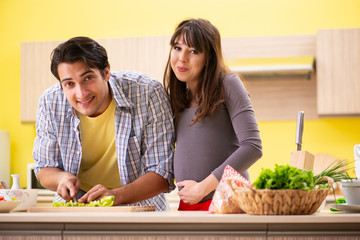 Man and pregnant woman preparing salad in kitchen 