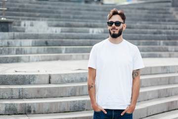 A young stylish man with a beard in a white T-shirt and glasses. Street photo