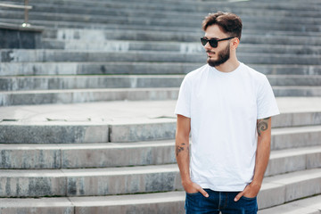 A young stylish man with a beard in a white T-shirt and glasses. Street photo