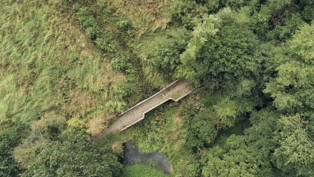 Aerial facing down view, spin move. Drone rotate over old small sandstone historic bridge, overgrown water pond in english countryside.