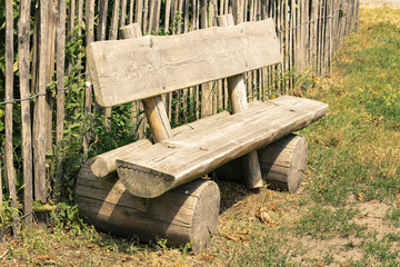 Fototapeta premium Bench, made of wood is in front of a wooden fence in countryside, during an arid summer