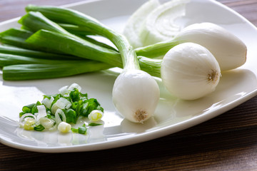 Three large Mexican onions which are green onions that have been allowed to grow bigger on a white plate with some smaller green onions sliced next to it on a kitchen table.