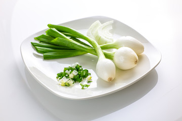 Three large Mexican onions which are green onions that have been allowed to grow bigger on a white plate with some smaller green onions sliced next to it on a kitchen table.