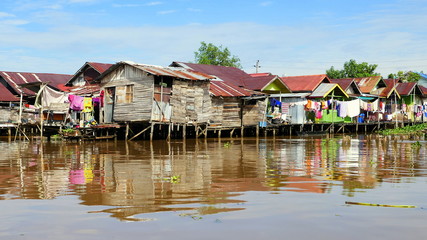 Fototapeta premium einfache Holzhütten stehen auf Pfählen im Fluss Martapura und spiegeln sich im Wasser