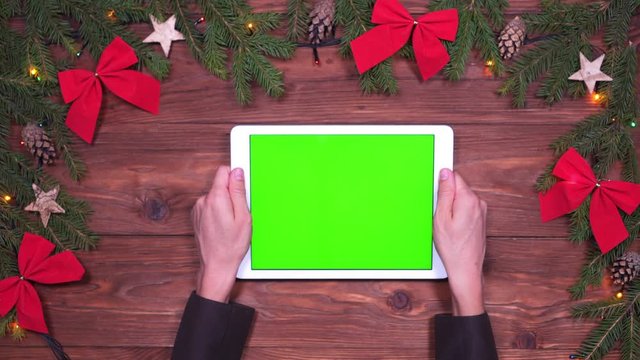 Hands holding digital tablet with green screen on Christmas background