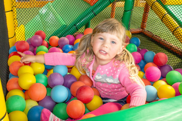 Girl playing and having a good time in a ball room on the playground. Happy playing and having fun at kindergarten with colorful balls, family weekend concept. Colorful ball bath for children.