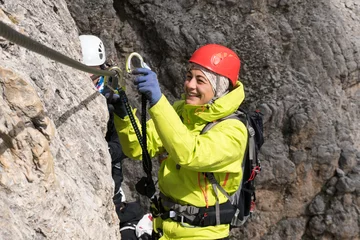 Foto op geborsteld aluminium Alpinisme young  female mountain climber on a Via Ferrata in the Dolomites in Alta Badia clicking carabiners in the cable for safety and smiling