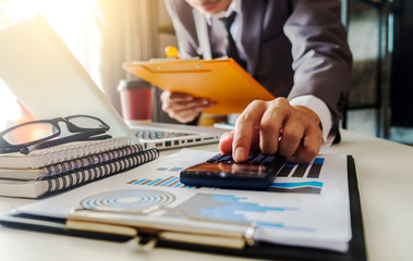 Fototapeta premium Businessman calculates financials with graph paper on the table on the cost of home office in the evening.