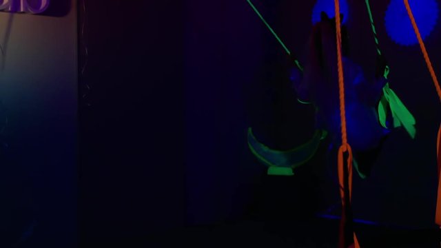 Young girl having fun on neon swing in dark room with UF light