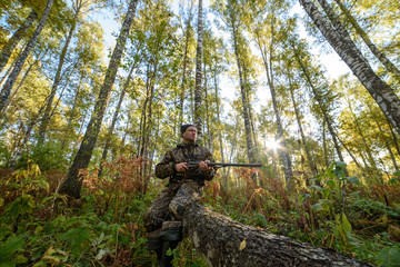 Hunter with a gun in the autumn forest against a background of trees with yellow foliage
