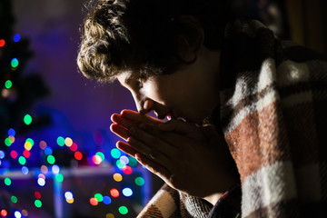 young teenager warm up hands sitting at home under blanket at winter night f