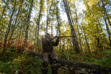 Hunter with a gun in the autumn forest against a background of trees with yellow foliage
