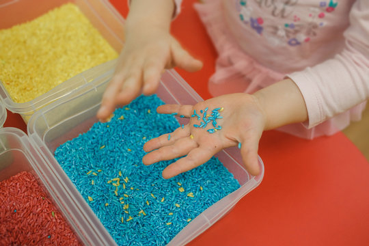 Child hands playing with colored rice in the sensory box. Baby's sensory educational kit