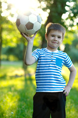 Portrait of a cute little boy with football sitting on grass in the park