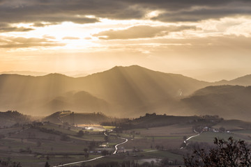 Fototapeta na wymiar Sunrays coming over a valley in Umbria (Italy) with some plants in the foreground