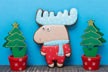 gingerbread or cookies in the shape of an elk on a blue background, near two decorative Christmas trees, the concept of Christmas