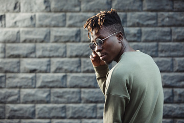 Fashionable man wearing modern clothes, male in pullover and glasses against brick wall