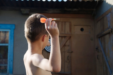 Teenager of boy holding a darts aiming at target in distance outdoor in yard. Child play game. ...