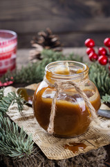 Homemade salted caramel sauce for christmas dessert in jar on rustic wooden table background. Copy space.