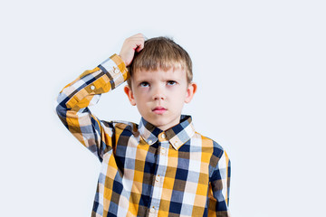 Little boy in a checked shirt on a white background thinks and puts his hand on his head
