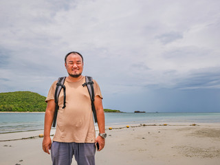 Asian fat Backpacker stand on the idyllic beach with Rainy cloud Sky in vacation time.Samae San Island thailand.Summer concept.