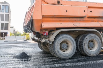 Ein Kipplaster bringt heißen Asphalt für die Erneuerung einer Fahrbahndecke einer Straße,...