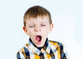 A male child in a plaid shirt on a white background yawns.
