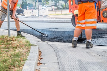 Straßenarbeiter verteilen den heißen Asphalt mit der Schaufel auf der Straße, Deutschland